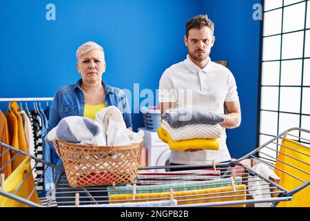 Hispanische Mutter und Sohn hängen Kleider an der Wäscheleine, skeptisch und nervös, Stirnrunzeln verärgert wegen des Problems. Negative Person. Stockfoto