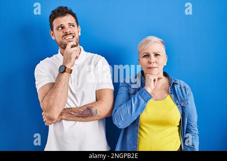 Junge brasilianische Mutter und Sohn stehen über blauem Hintergrund und denken besorgt über eine Frage, besorgt und nervös mit der Hand am Kinn Stockfoto
