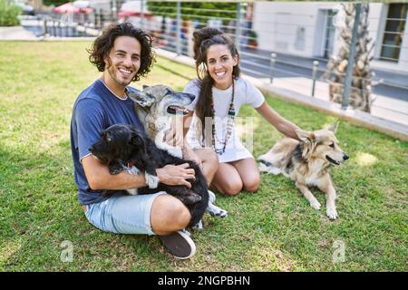 Mann und Frau Paar lächeln selbstbewusst auf Kraut mit Hunden im Park sitzen Stockfoto