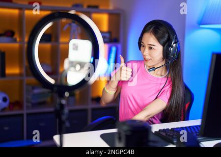 Junge chinesin nimmt Vlog-Tutorial mit Smartphone zu Hause auf und lächelt glücklich und positiv, Daumen hoch, ausgezeichnet und Bestätigung unterschreiben Stockfoto