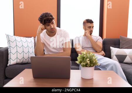 Zwei lateinamerikanische Männer sitzen zu Hause auf dem Sofa und haben traurige Ausdrücke Stockfoto