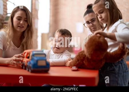 Lehrer mit Jungen und Mädchen, die mit Autos spielen, Spielzeug und Puppe, die im Kindergarten auf dem Tisch sitzt Stockfoto