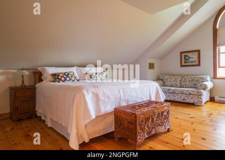 Kingsize-Bett mit geschnitzter, exotischer Holzkiste und gepolstertem Sofa im Hauptschlafzimmer mit Kiefernholzböden auf der oberen Etage im 1990er. Haus. Stockfoto