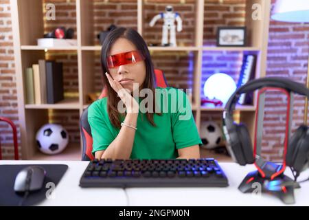 Eine chinesin mittleren Alters, die eine Virtual-Reality-Brille trägt und denkt, müde und gelangweilt auszusehen, mit Depressionsproblemen mit gekreuzten Armen. Stockfoto