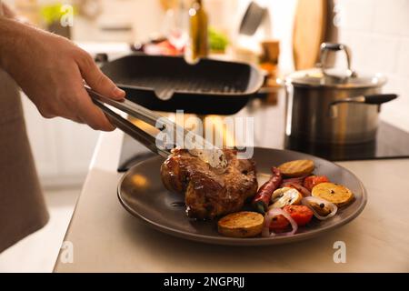 Ein Mann, der Fleisch auf den Teller legt, mit Gemüse, das in der Bratpfanne gekocht wurde, Nahaufnahme Stockfoto