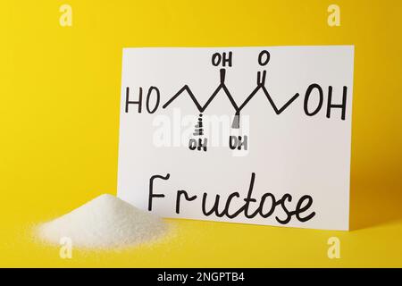 Ein Haufen Zucker und das Wort Fructose mit gezeichnetem Schema auf Papier auf gelbem Hintergrund Stockfoto