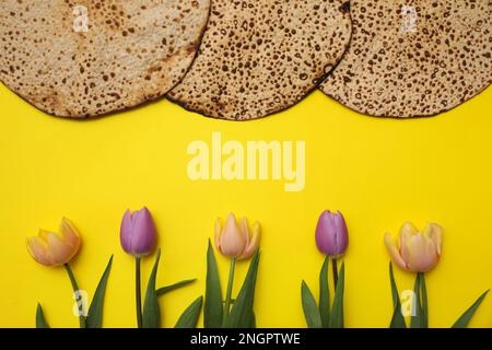 Leckere Matzen und frische Blumen auf gelbem Hintergrund, flach liegend. Pessach-Feier Stockfoto