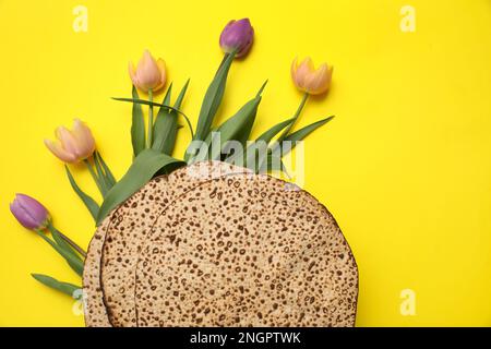 Leckere Matzen und frische Blumen auf gelbem Hintergrund, flach liegend. Pessach-Feier Stockfoto