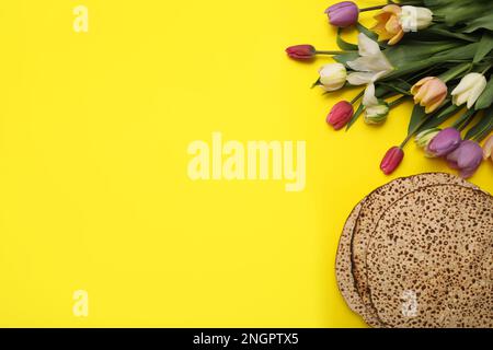 Leckere Matzen und frische Blumen auf gelbem Hintergrund, flach liegend mit Platz für Text. Pessach-Feier Stockfoto