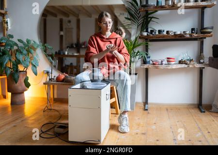 Die Meisterin der Töpferei wischt die Hände vom Lehm ab, nachdem sie in der Werkstatt an einem speziell angefertigten Keramikprodukt gearbeitet hat. Stockfoto