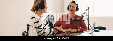 Eine weibliche Radio-Moderatorin interviewt einen Gast in ihrer Show in ihrem Heimstudio. Zwei Frauen, die sich unterhalten und gleichzeitig eine Live-Audioübertragung moderieren Stockfoto