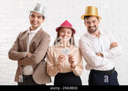 Kollegen und Papier mit Text HAPPY IDIOTEN'S DAY auf weißem Ziegelhintergrund Stockfoto