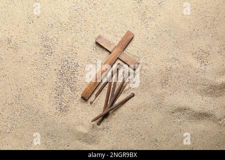 Holzkreuz mit Nägeln auf Sand. Karfreitagskonzept Stockfoto