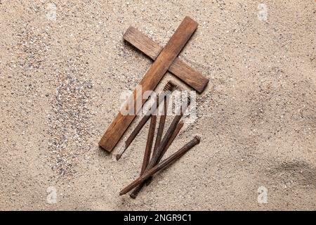 Holzkreuz mit Nägeln auf Sand. Karfreitagskonzept Stockfoto