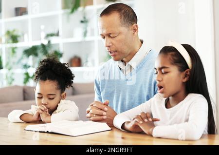 Familie, Gottesdienst und bibel mit Vater und Kindern, die am Tisch für Frieden, Religion und Glauben in ihrem Zuhause beten. Gott, bete für Kinder mit Eltern Stockfoto