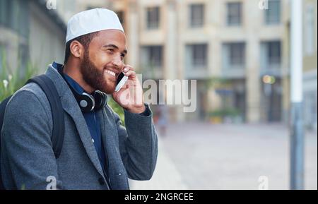 Muslimischer Geschäftsmann, der in der Stadt mit einem Smartphone telefoniert und glücklich lächelt Stockfoto