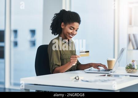 Es ist an der Zeit, dass wir alle zum Online-Banking wechseln. Eine junge Geschäftsfrau, die ihren Laptop und ihre Kreditkarte in einem modernen Büro benutzt. Stockfoto