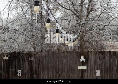 Nahaufnahme von Eiszapfen auf der Terrasse Partylichtern mit Eis, das den Baum im Hintergrund bedeckt. Wintersturm in Austin, TX Stockfoto