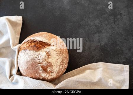 Frisch gebackene Brotlaibe mit Küchenhandtuch auf schwarzem Hintergrund. Draufsicht. Speicherplatz kopieren Stockfoto
