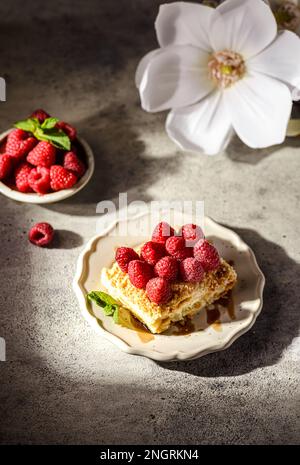 napoleonkuchen auf grauem Hintergrund. Der Kuchen besteht aus Blätterkuchen mit Vanille und ist mit frischen Himbeeren dekoriert Stockfoto