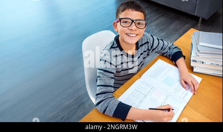 Auf der Suche nach Wissen. Porträt eines entschlossenen Jungen, der seine Hausaufgaben zu Hause macht. Stockfoto