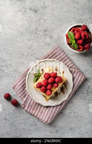 napoleonkuchen auf grauem Hintergrund. Der Kuchen besteht aus Blätterkuchen mit Vanille und ist mit frischen Himbeeren dekoriert Stockfoto