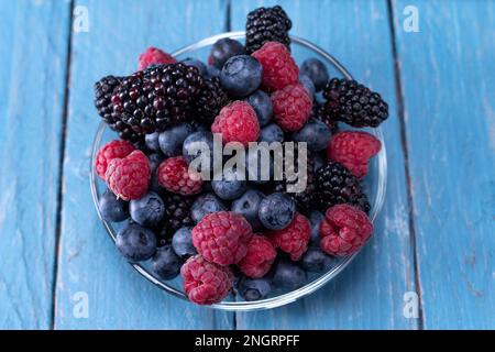 Verschiedene Waldbeeren auf einer Glasplatte. Mehrfarbige Beeren in einer Untertasse. Sommerwaldbeeren auf einem Teller auf dem Tisch. Blick von oben. Stockfoto