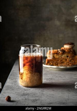 Ein Glas Kaffee mit Milch. Milch wird in den Kaffee gegossen, und Muster erscheinen. Ein Kinderspiel im Hintergrund Stockfoto