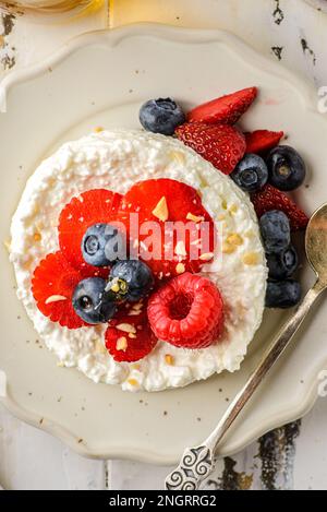 Hüttenkäse mit Himbeeren, Erdbeeren und Heidelbeeren. Hüttenkäse wird in Form eines Gebäckrings neben einem Glas Honig und Cho aufgemacht Stockfoto