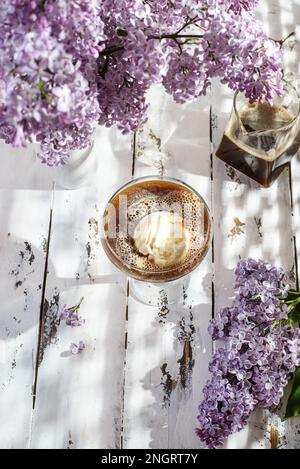 Eis ist in einem Glas, neben Kaffee und Flieder. Glasse Kaffee besteht aus Eiscreme und Espresso Stockfoto