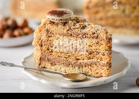 Baiser-Kuchen mit Nusscreme. Stücke Esterhazy-Kuchen auf hellem Hintergrund, neben Tee und Haselnüssen Stockfoto