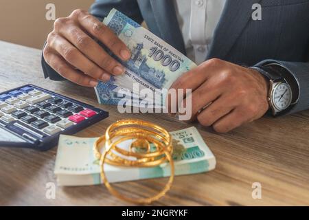 Ein Geschäftsmann, der mit pakistanischen Ehebrechern mit Währungsscheinen und Gold zu tun hat, um Geld zu sparen, Investitionen zu tätigen und die Finanzbuchhaltung zu verwalten oder zu wachsen Stockfoto
