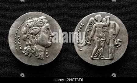 Alte griechische Münze, Makroansicht des Geldes mit menschlichem Porträt und geflügeltem gott. Alte seltene Münze isoliert auf dunklem Hintergrund. Thema Griechenland, Hellenistisch, A Stockfoto