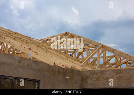 Unlackierte Putzwände und Holzdachbalken eines im Bau befindlichen Hauses mit Gewitterwolken im Hintergrund. Stockfoto