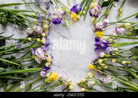 Rahmen aus verschiedenen Blumen auf Marmorhintergrund. Flach liegend, Draufsicht, Kopierbereich. Osterkomposition. Romantisches saisonales Designelement. Herzlichen Glückwunsch Stockfoto