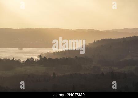 Wunderschöne Wintersonnenaufgangslandschaft von Loughrigg auf Windermere mit atemberaubenden Sonnenstrahlen aus den dunklen Wolken Stockfoto