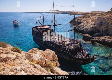 Touristenpiratenschiff neben dem Steinbogen Kamara tou Koraka im Cape Greco National Forest Park in Zypern Stockfoto