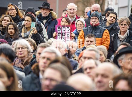 Hanau, Deutschland. 19. Februar 2023. Eine Frau (M) hält bei einer Gedenkfeier auf dem Marktplatz ein Plakat mit Bildern der Opfer in der Hand, auf dem die neun Opfer des rassistischen Angriffs in Hanau vor drei Jahren geehrt werden. Ein 43-jähriger Deutscher hatte neun Menschen aus rassistischen Motiven erschossen und dann seine Mutter und sich selbst getötet. Kredit: Frank Rumpenhorst/dpa/Alamy Live News Stockfoto