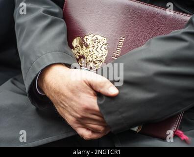 Hanau, Deutschland. 19. Februar 2023. Claus Kaminsky (SPD), der Bürgermeister von Hanau, sitzt neben den Angehörigen der Opfer mit einem offiziellen Ordner aus der Stadt bei einer Gedenkfeier auf dem Marktplatz, um an die neun Opfer des rassistischen Angriffs in Hanau vor drei Jahren zu erinnern. Ein 43-jähriger Deutscher hatte neun Menschen aus rassistischen Motiven erschossen und dann seine Mutter und sich selbst getötet. Kredit: Frank Rumpenhorst/dpa/Alamy Live News Stockfoto