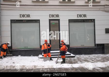 Moskau, Russland. 17. Februar, 2023. Arbeiter säubern Schnee vor dem Hintergrund eines geschlossenen Outlets von Dior in der Stoleshnikov Lane im Zentrum von Moskau, Russland Stockfoto