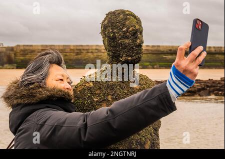 Margate, Großbritannien. 17. Februar 2023 Besucher besuchen Antony Gormley: Ein anderes Mal, am Nayland Rock, neben dem Turner Contemporary, in Margate. Das Werk wird erst enthüllt, wenn die Flut zurückgeht. Es ist eine von hundert soliden gusseisernen Figuren von Antony Gormley, die die Erfahrung des menschlichen Wesens erforschen. Leben an der Margate Küste. Kredit: Guy Bell/Alamy Live News Stockfoto