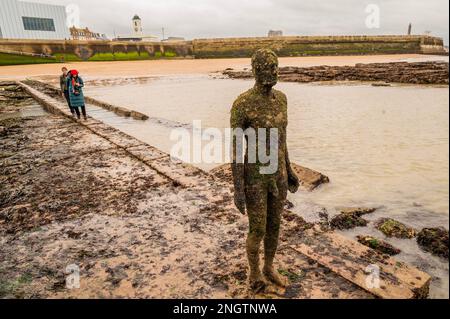Margate, Großbritannien. 18. Februar 2023 Besucher besuchen Antony Gormley: Ein anderes Mal, am Nayland Rock, neben dem Turner Contemporary, in Margate. Das Werk wird erst enthüllt, wenn die Flut zurückgeht. Es ist eine von hundert soliden gusseisernen Figuren von Antony Gormley, die die Erfahrung des menschlichen Wesens erforschen. Leben an der Margate Küste. Kredit: Guy Bell/Alamy Live News Stockfoto