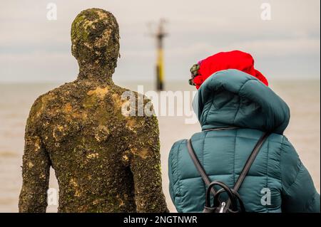 Margate, Großbritannien. 18. Februar 2023 Besucher besuchen Antony Gormley: Ein anderes Mal, am Nayland Rock, neben dem Turner Contemporary, in Margate. Das Werk wird erst enthüllt, wenn die Flut zurückgeht. Es ist eine von hundert soliden gusseisernen Figuren von Antony Gormley, die die Erfahrung des menschlichen Wesens erforschen. Leben an der Margate Küste. Kredit: Guy Bell/Alamy Live News Stockfoto