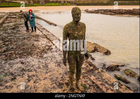 Margate, Großbritannien. 18. Februar 2023 Besucher besuchen Antony Gormley: Ein anderes Mal, am Nayland Rock, neben dem Turner Contemporary, in Margate. Das Werk wird erst enthüllt, wenn die Flut zurückgeht. Es ist eine von hundert soliden gusseisernen Figuren von Antony Gormley, die die Erfahrung des menschlichen Wesens erforschen. Leben an der Margate Küste. Kredit: Guy Bell/Alamy Live News Stockfoto