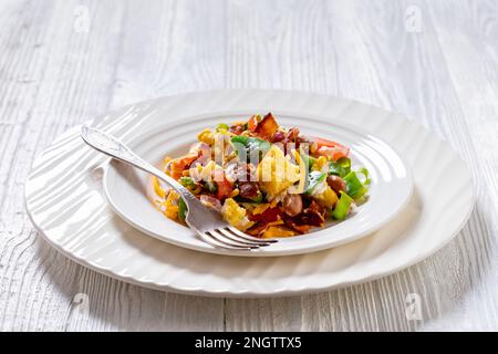 Nahaufnahme von Pinto Beans Speck Maisbrotsalat mit Tomaten, Paprika, Mais und Cheddar Käse auf einem Teller aus weißem Holz, horizontale Ansicht von oben Stockfoto