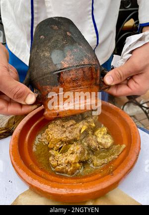 Ein Mann gießt Tangia, Tanjia, gebratenes Lamm, gekocht in Tontöpfen, in eine Keramikplatte. Marrakesch, Marokko. Stockfoto