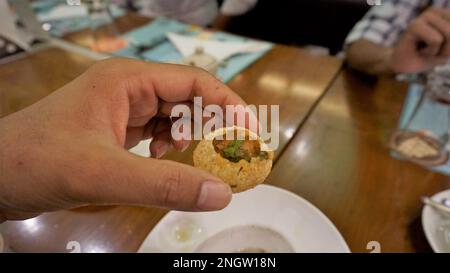 Ein indischer Mann hält Panipuri oder Golgappa oder Puchkas mit Kartoffelmasala drin. Ein beliebtes indisches Chat-Menü. Stockfoto