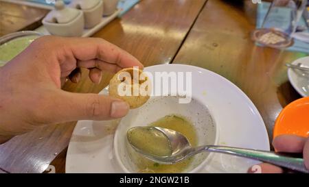 Ein indischer Mann hält Panipuri oder Golgappa oder Puchkas mit Kartoffelmasala und gießt Pani mit silbernem Löffel hinein. Stockfoto