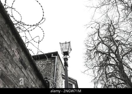 Rasierdraht an einer Außenwand neben einem schmiedeeisernen Laternenpfahl in Großbritannien. Ein Problembereich mit antisozialem Verhalten und Drogenhandel. Stockfoto