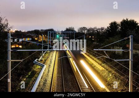 Hochgeschwindigkeitszug auf Gleisen mit Bewegungsunschärfe bei Sonnenuntergang. Pendlerstrecke in Cardiff, Wales. Stockfoto